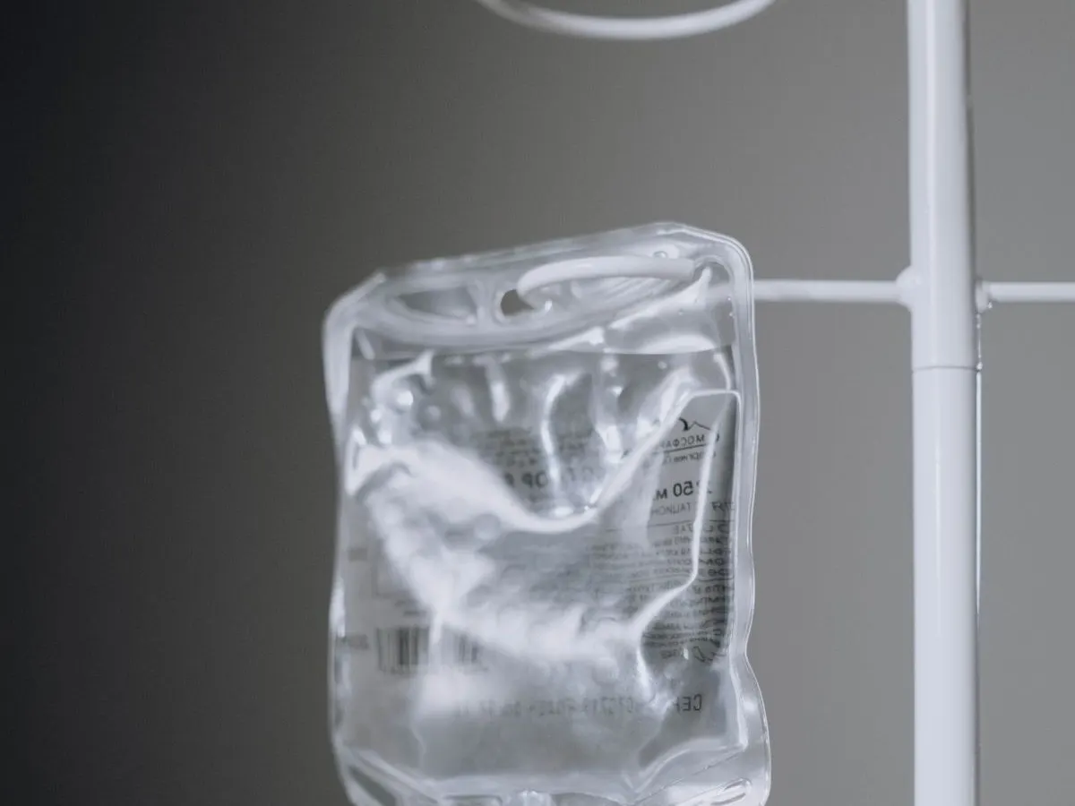 An IV bag hanging from a stand, lit against a dark background