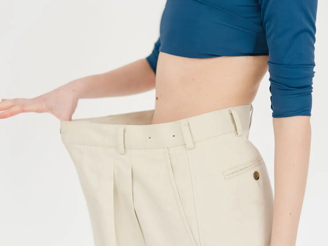 A person holding out the loose waistband of trousers that no longer fit
