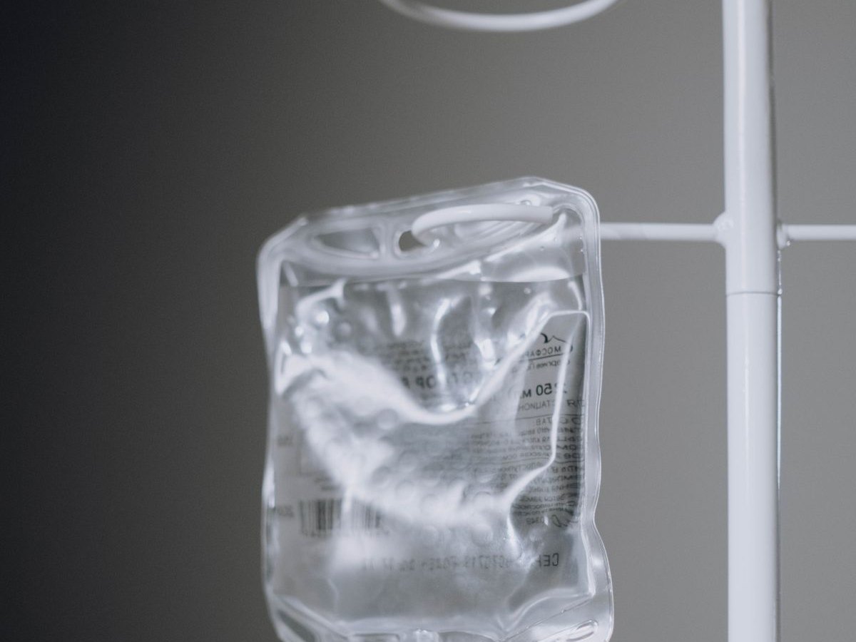 An IV bag hanging from a stand, lit against a dark background