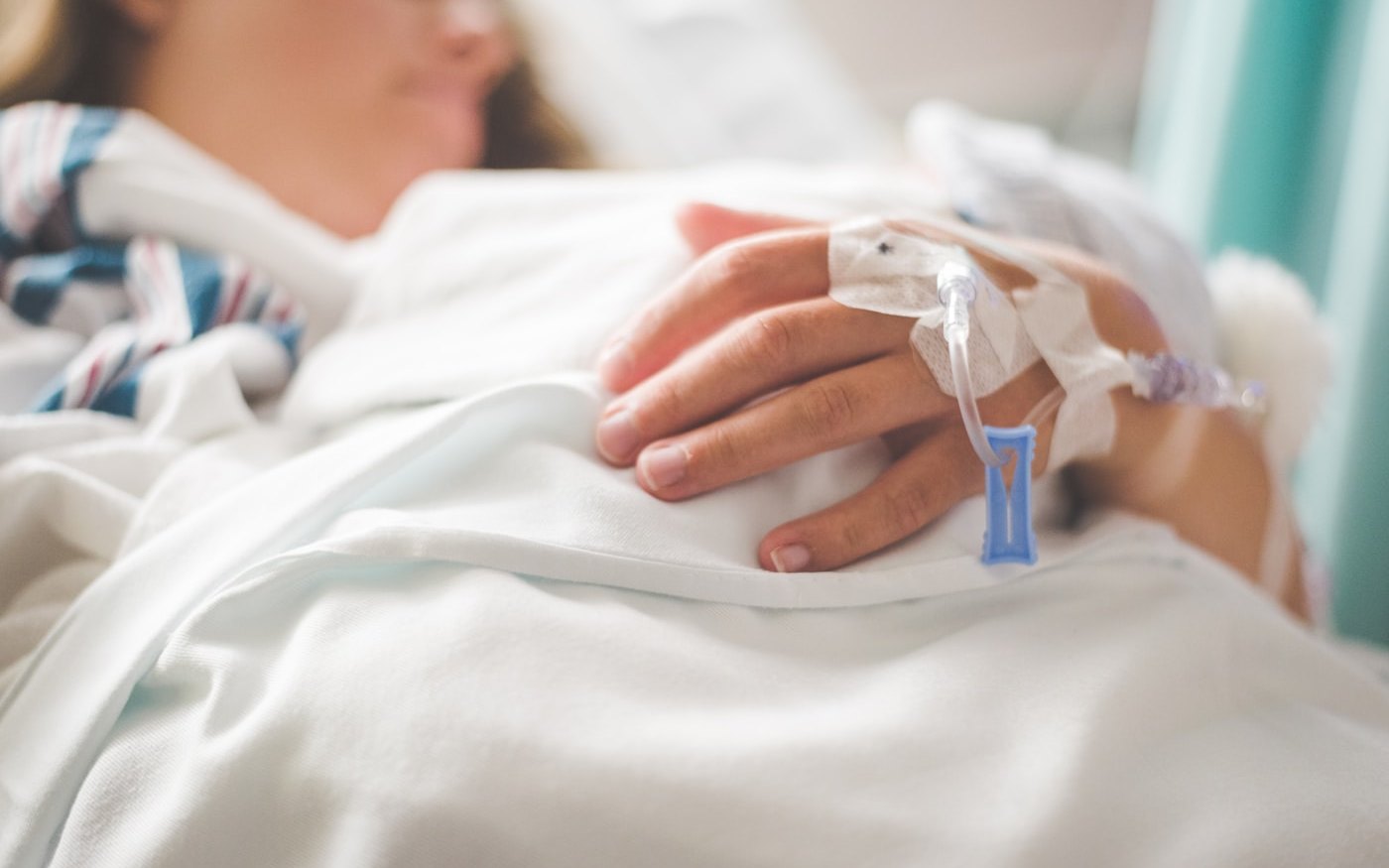 A cannula taped to a patient's hand, resting on white bedding during an infusion