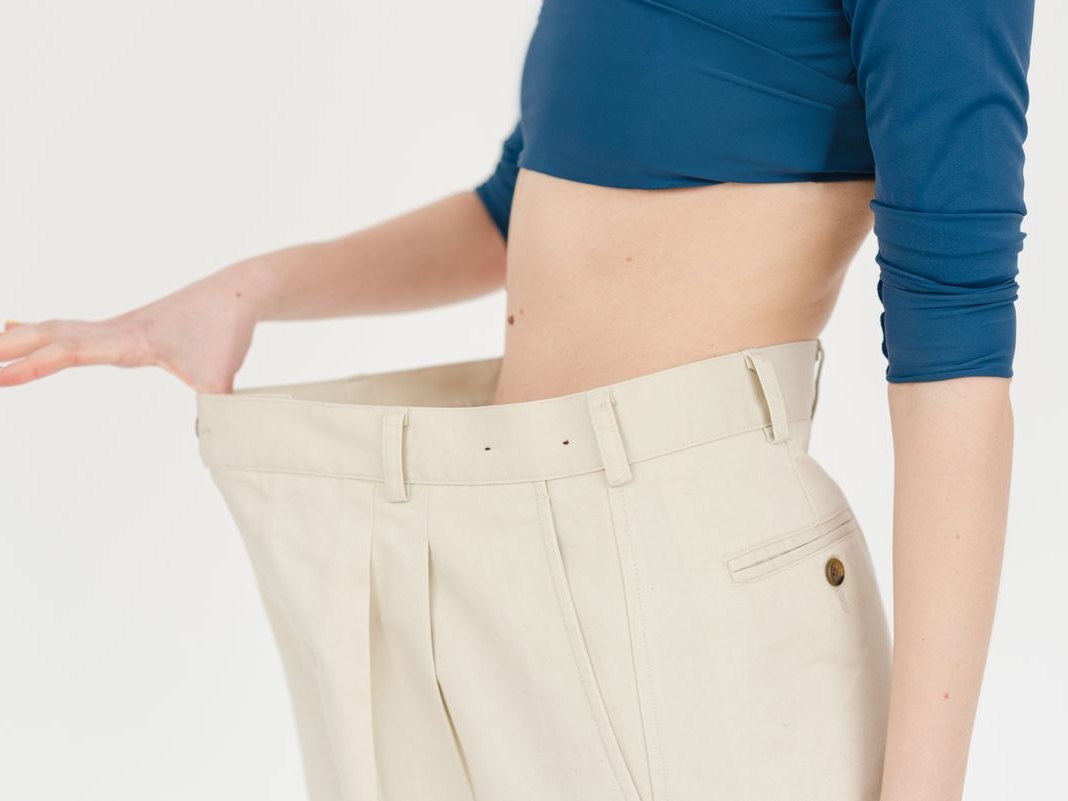 A person holding out the loose waistband of trousers that no longer fit